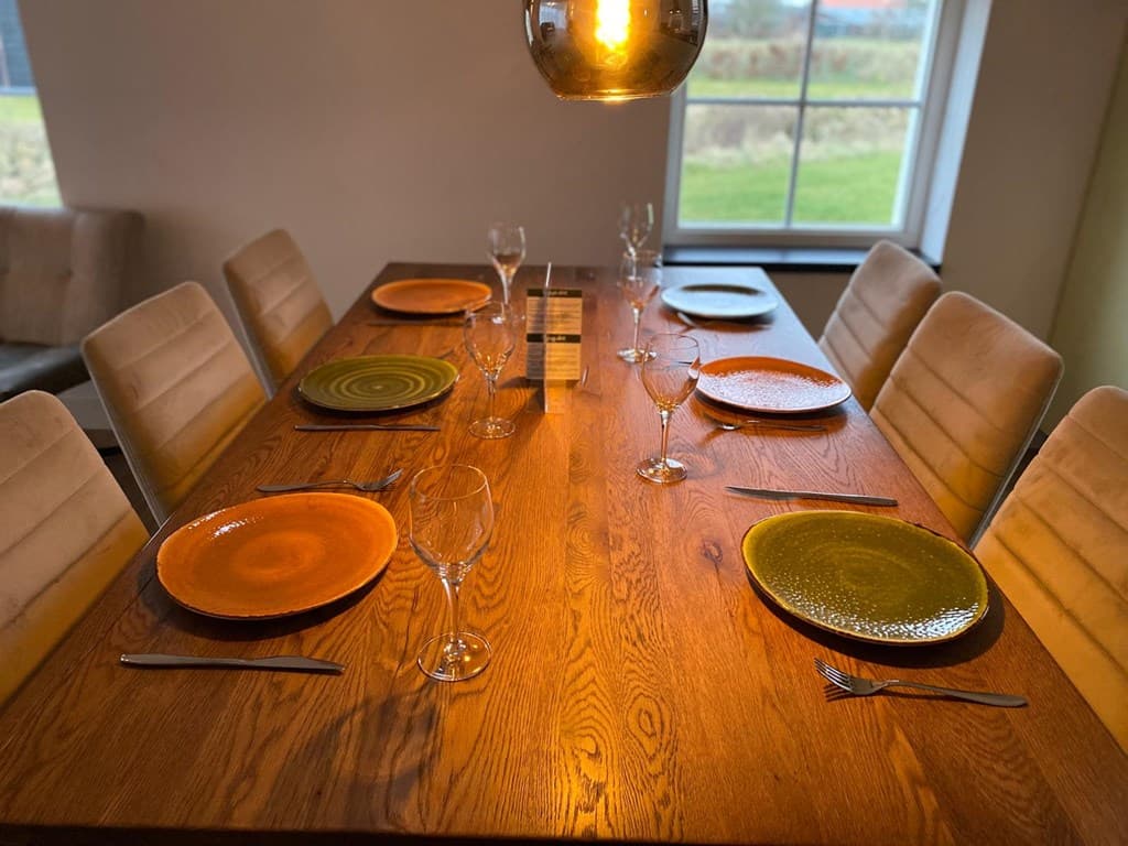Eettafel met zes borden, glazen en bestek, aan de muur een groot raam met uitzicht op het grasland.