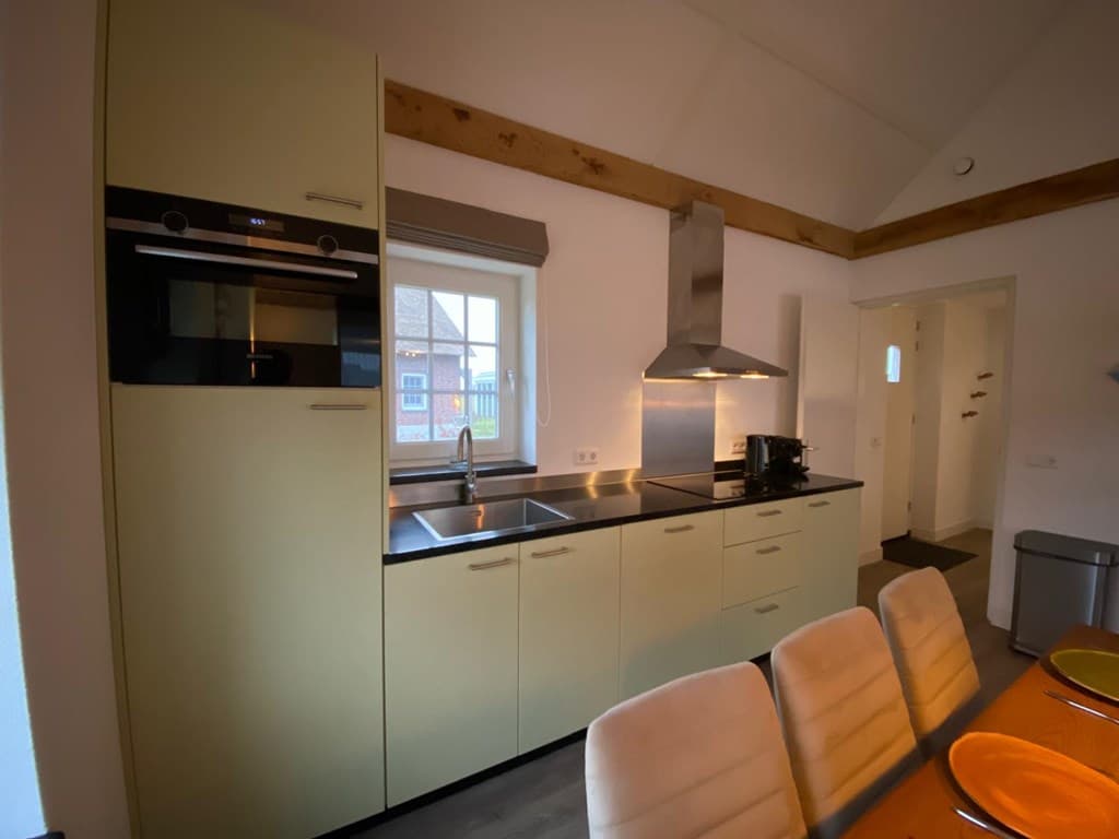 Moderne keuken met lichte kasten, een keukenblad van zwart staal en een eettafel met beige stoelen.