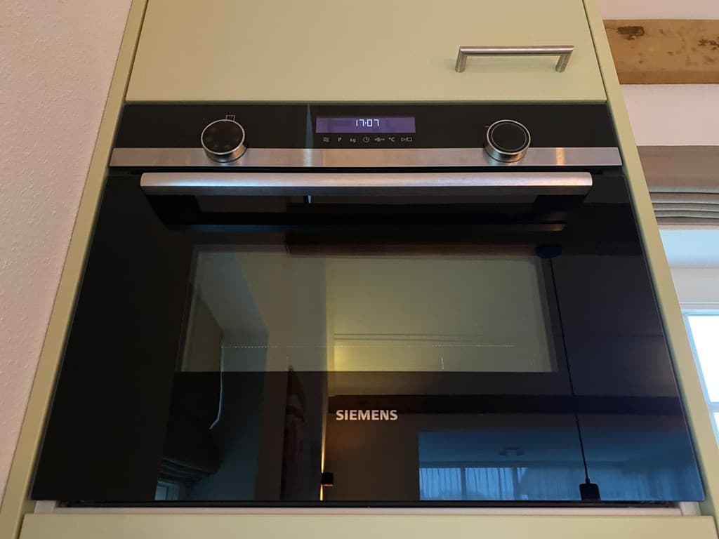 Zwarte inbouwoven van het merk Siemens in een keuken met lichte kastjes.