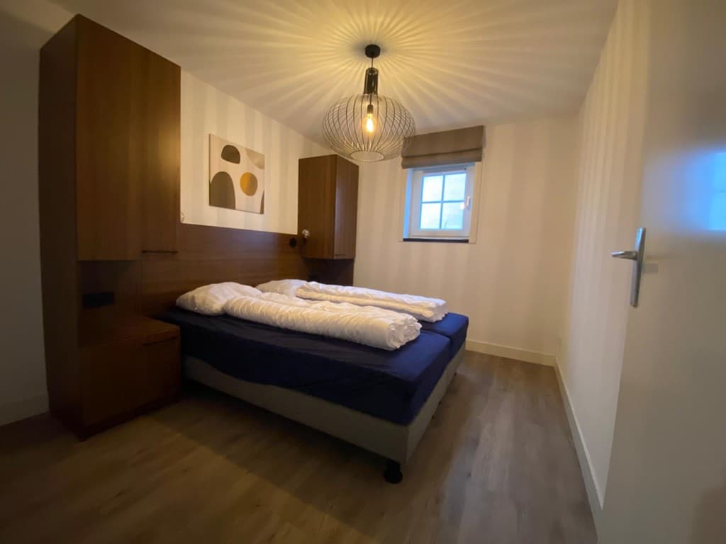 Slaapkamer met een tweepersoonsbed, wandkasten en een moderne lamp aan het plafond.