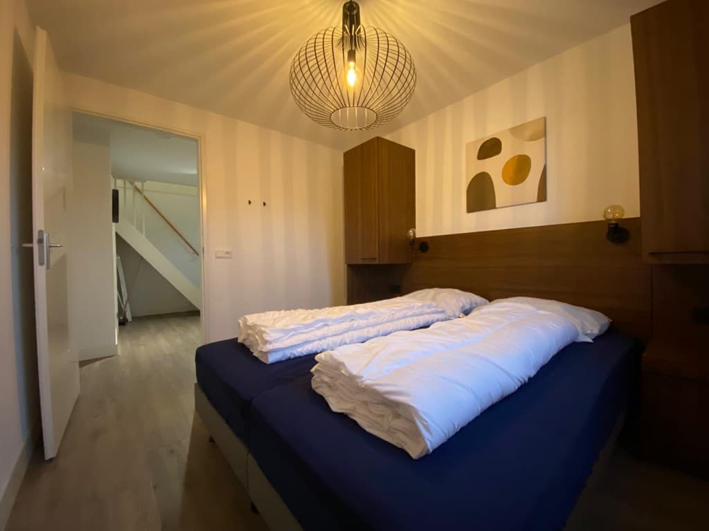 Slaapkamer met twee losse bedden, houten kasten en een moderne lamp aan het plafond
