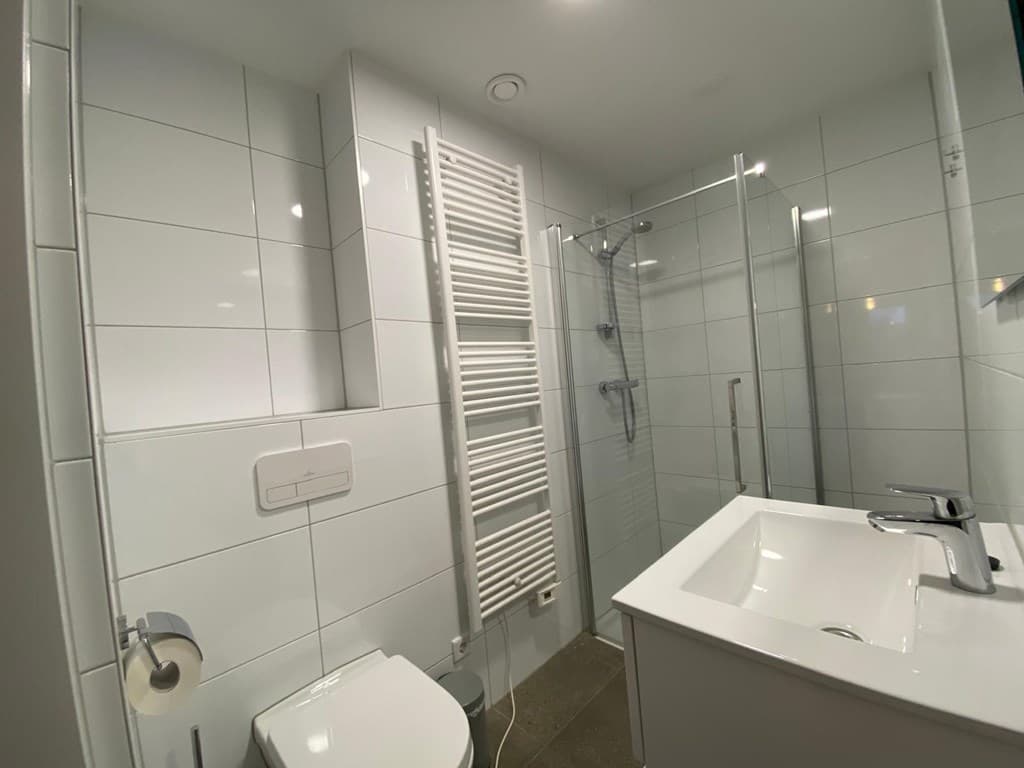 Moderne badkamer met inloopdouche, toilet, wastafel en radiator met witte tegels aan de muren