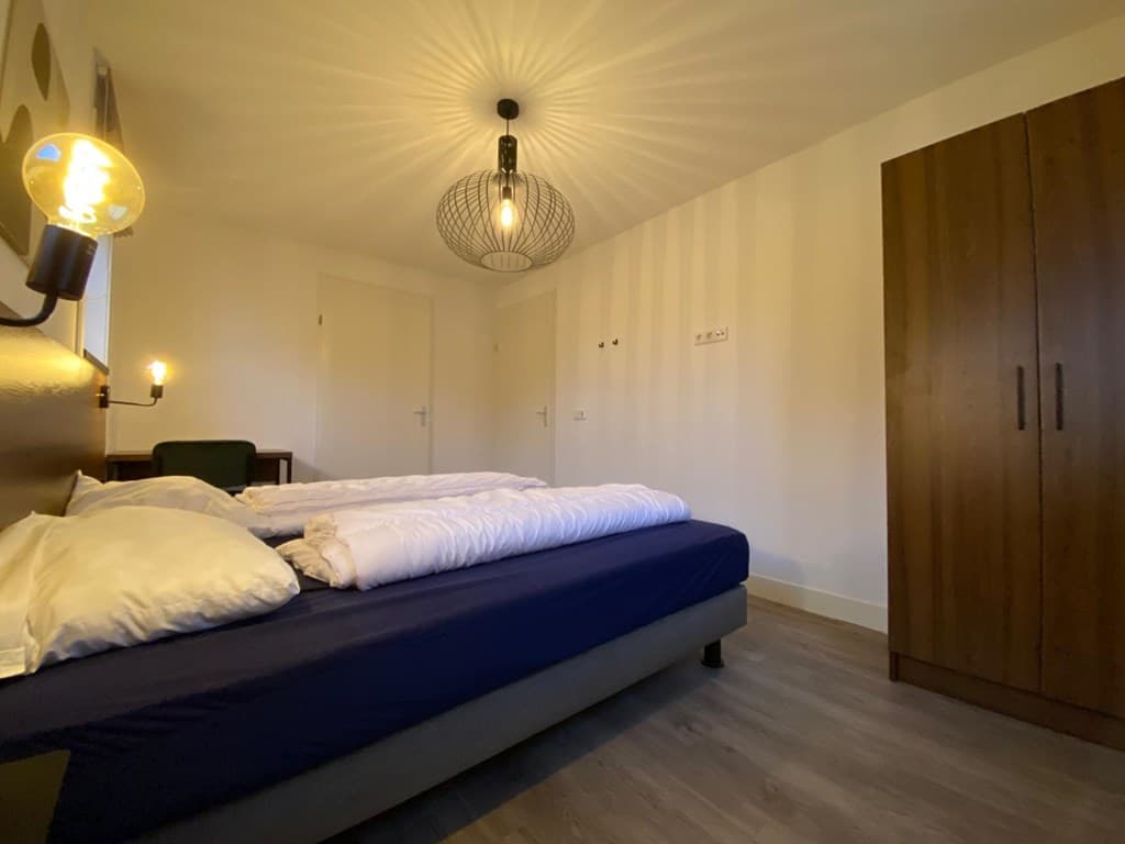 Slaapkamer met een groot bed, een kast en een hanglamp aan het plafond.