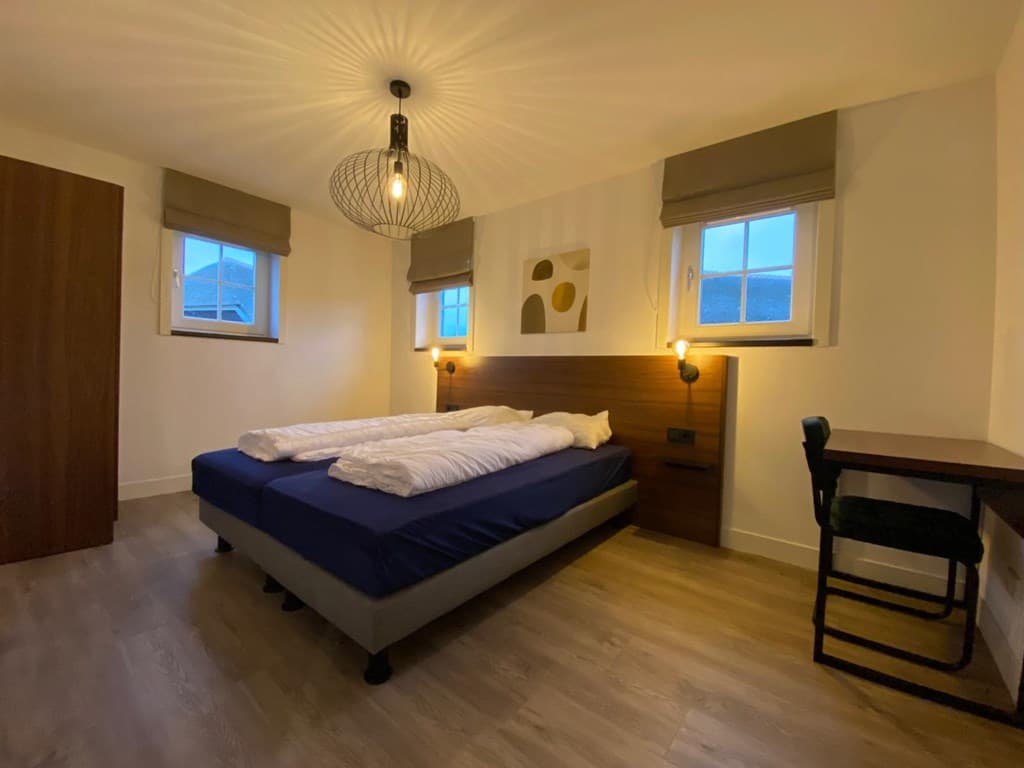 Ruime slaapkamer met twee aparte bedden, bureau en moderne verlichting, rondom ramen met elektrische zonwering.