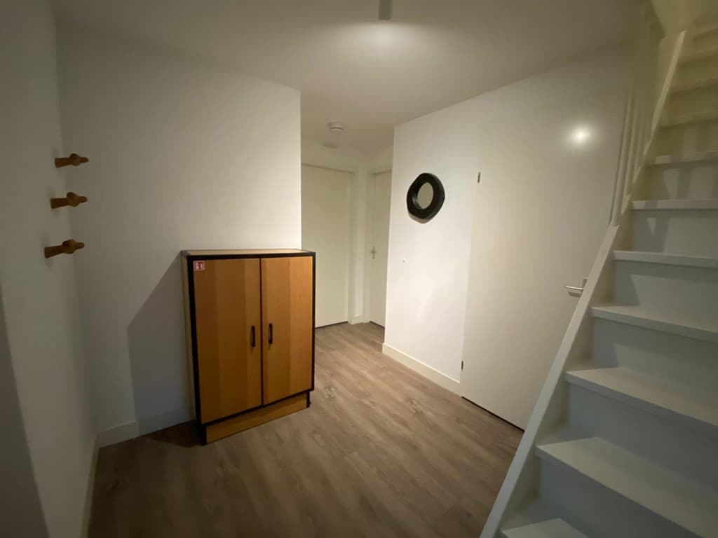 Ingang van de woning met een kast, muurhaken en een trap naar een bovenverdieping.
