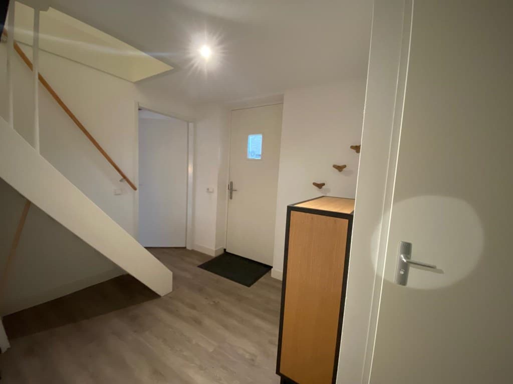 Entree van de woning met trap, deur naar buiten en kast met enkele decoratieve elementen aan de muur