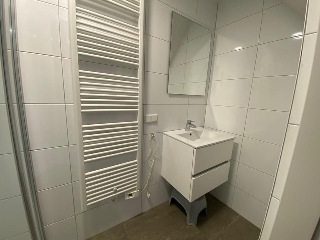 Moderne badkamer met witte tegels, wastafel met lade en spiegel, handdoekenradiator en inloopdouche.