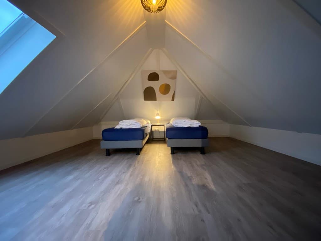 Slaapkamer met twee aparte bedden, houten vloer en schuin dak met dakramen en een lamp aan het plafond.