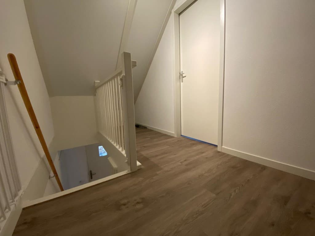 Overloop met houten vloer en trapleuningen, toegang tot een deur aan het einde van de gang.