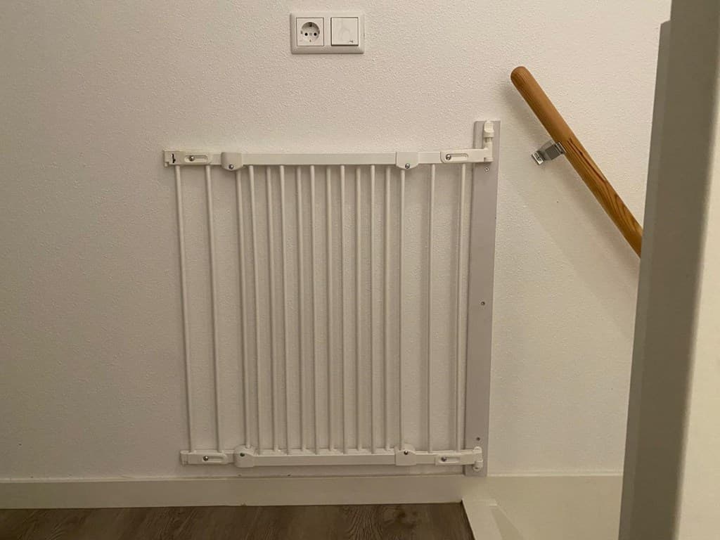 Traphekje aan de muur bij de trap met een houten leuning en een stopcontact erboven.