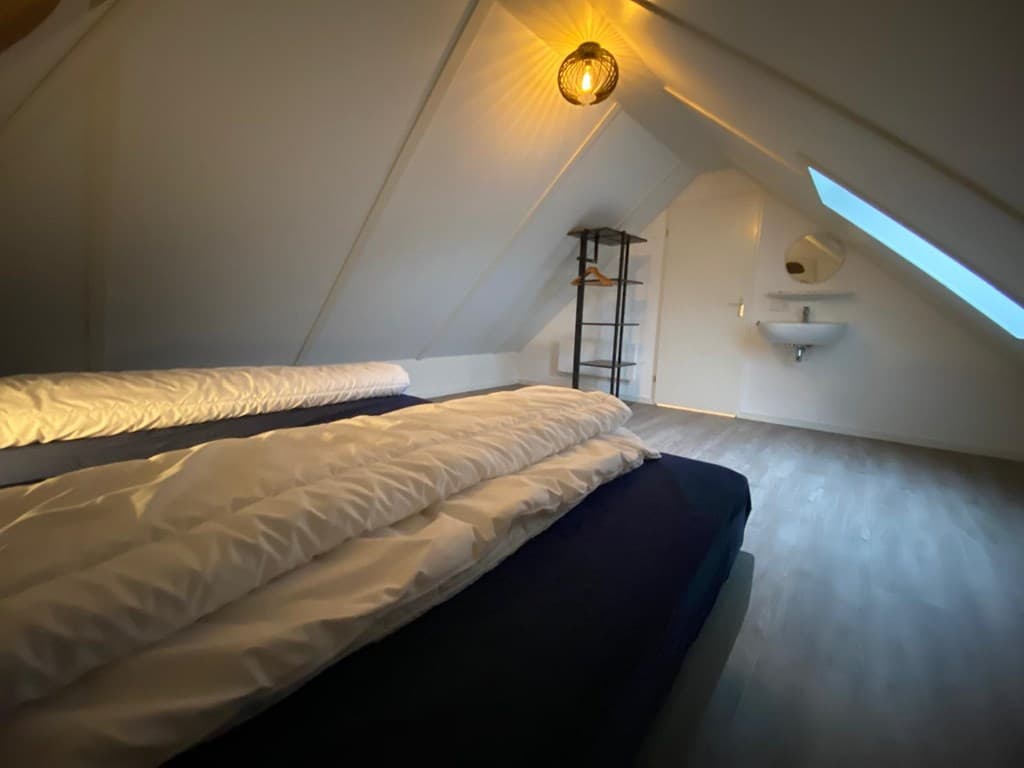 Sfeervolle zolderkamer met schuin dak, tweepersoonsbed en wastafel nabij het raam