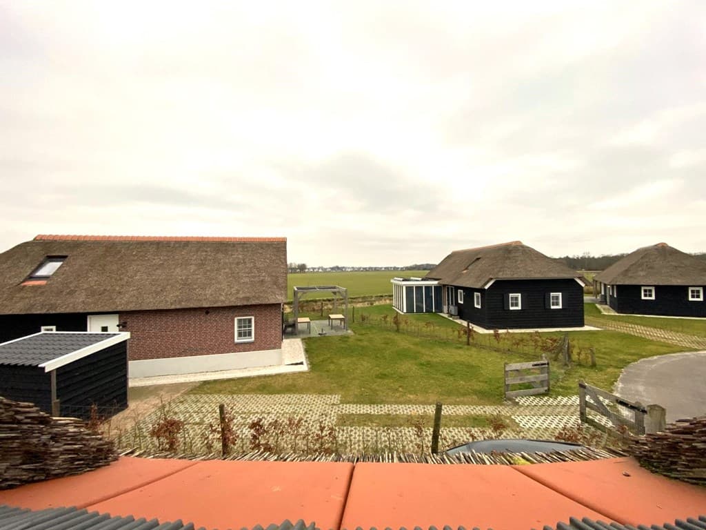 Uitzicht op twee vakantiewoningen met rieten daken en een groene tuin tussen de woningen en het verdriet