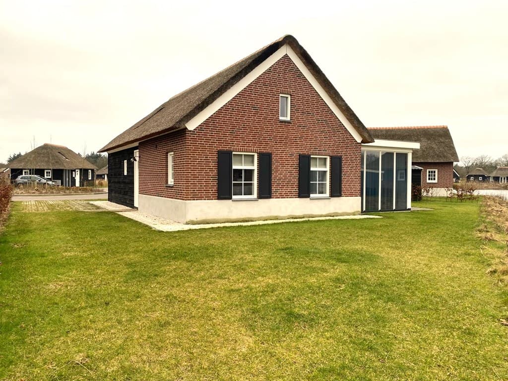 Vrijstaande vakantiewoning met rieten dak, rode bakstenen gevel en grasveld rondom het huis.