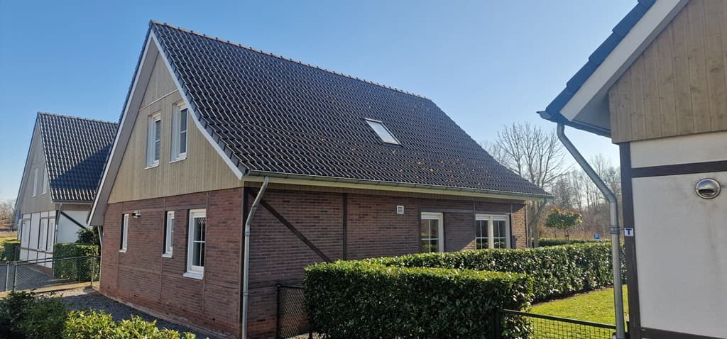 Tweelaags vakantiehuis met houten en metselwerk, groene heg en heldere lucht op EuroParcs Limburg in Susteren