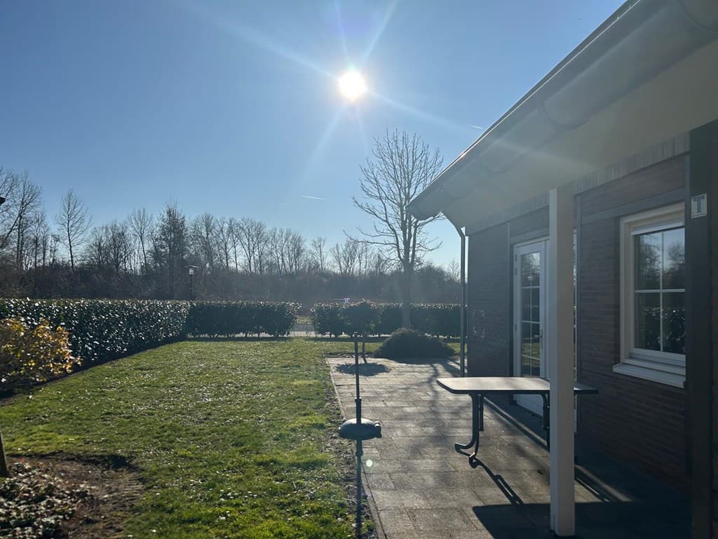 Tuin met gras en een tafel, bij zonnig weer met heldere lucht en bomen op de achtergrond.
