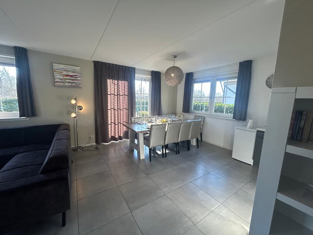 In een lichte woonkamer met een eettafel voor zes personen, een bank en grote ramen met uitzicht op de tuin.