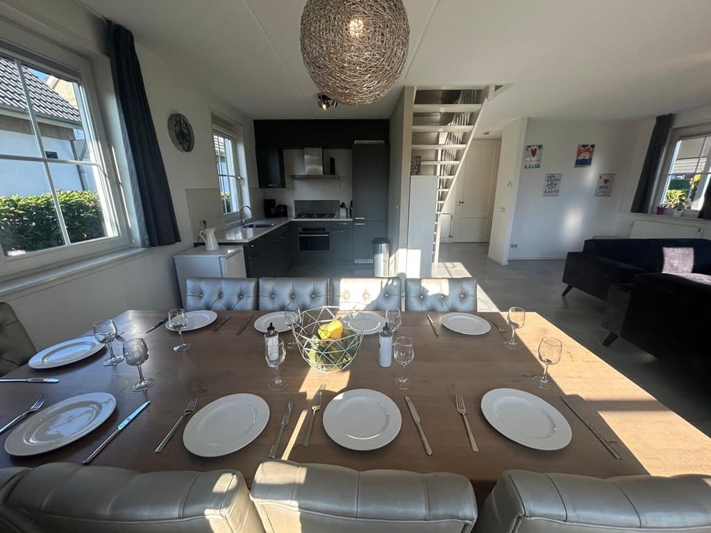Eetkamer met lange tafel, moderne keuken in de achtergrond en zithoek met bank in een lichte woonkamer