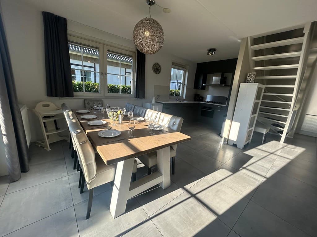 Ruim eetgedeelte met een lange tafel en stoelen, uitzicht op de open keuken en een trap naar boven