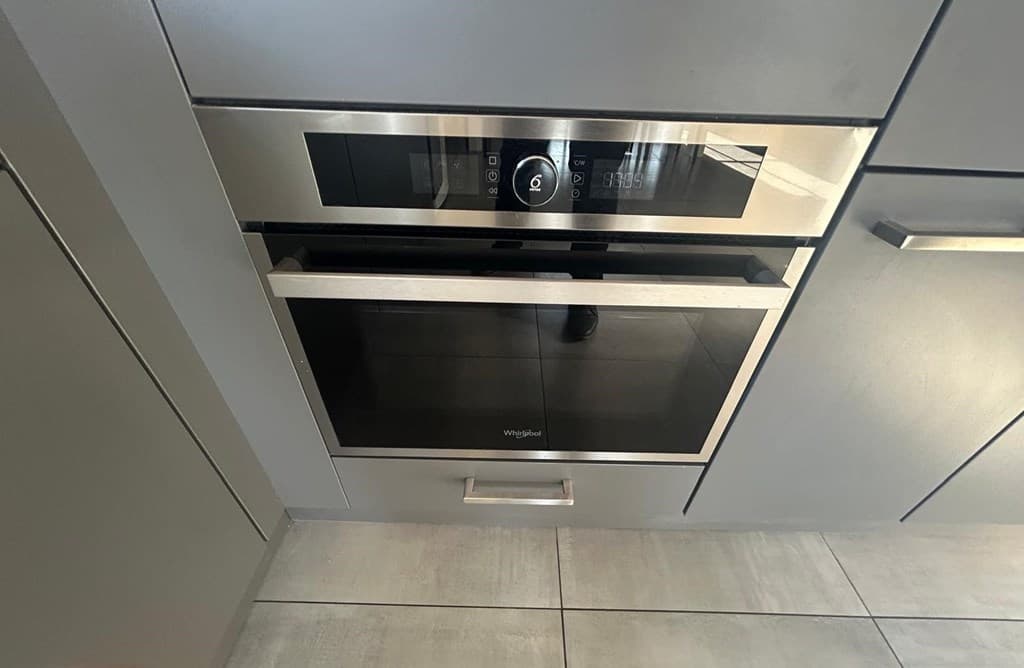 Ingebouwde oven met een zwarte deur en bedieningspaneel in een moderne, grijze keukenkast.