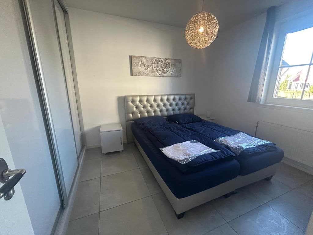 Slaapkamer met tweepersoonsbed, moderne verlichting en grote raampartij voor natuurlijk licht.