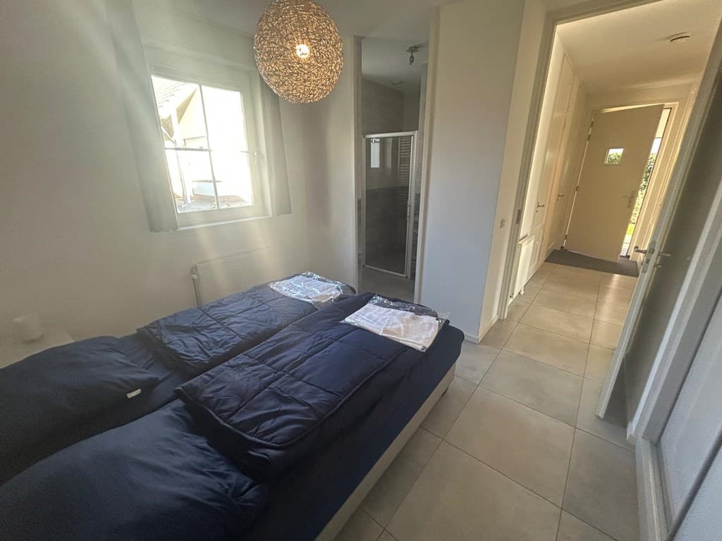 Slaapkamer met twee losse bedden, natuurlicht en een deur naar een badkamer met douchegedeelte.