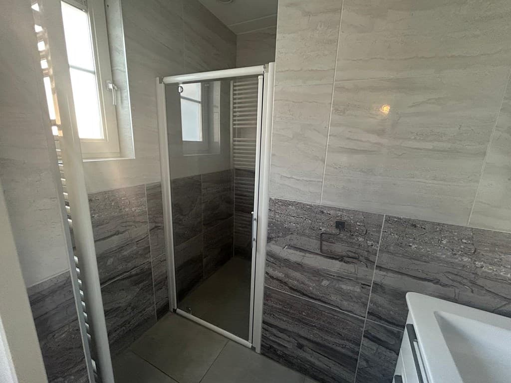 Moderne badkamer met een glazen inloopdouche, wastafel en tegels in neutrale kleuren.