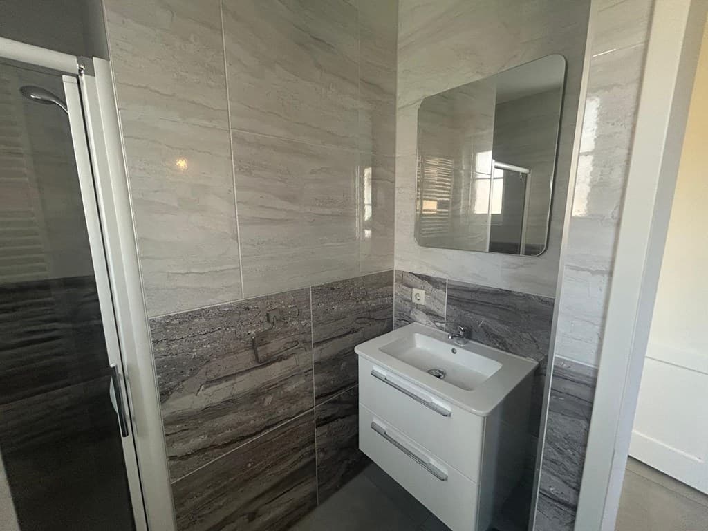 Moderne badkamer met douche, wastafel en spiegel, betegelde wanden in neutrale kleuren