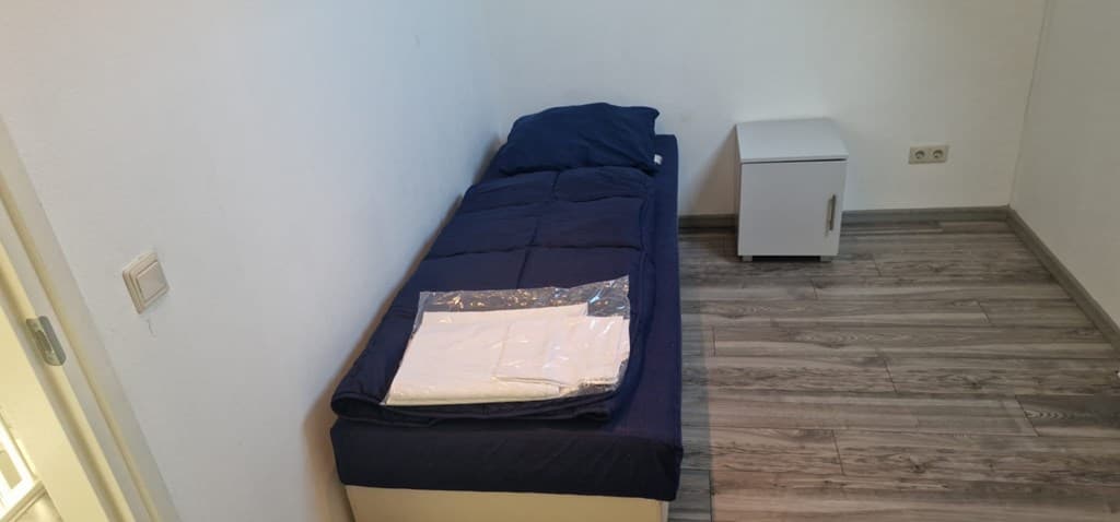 Een slaapkamer met een eenpersoonsbed, een nachtkastje en een opgemaakte bedden.