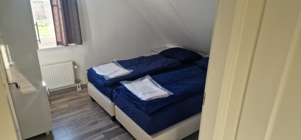 Slaapkamer met twee enkele bedden, blauwe dekbedden en een raam met gordijnen
