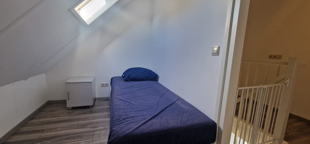 Slaapkamer onder het schuine dak met een eenpersoonsbed en een nachtkastje naast het bed