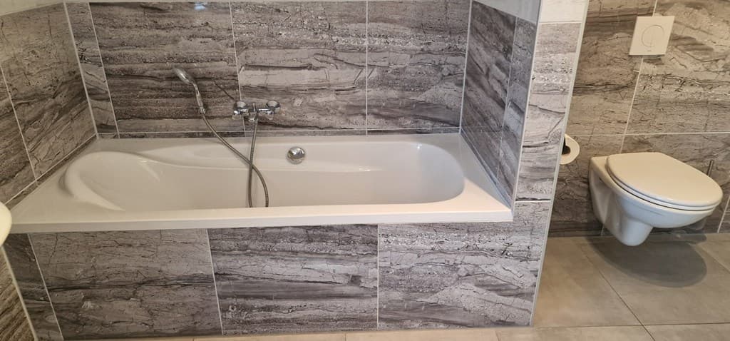 Badkamer met een ligbad, wc en betegelde wanden in neutrale kleuren