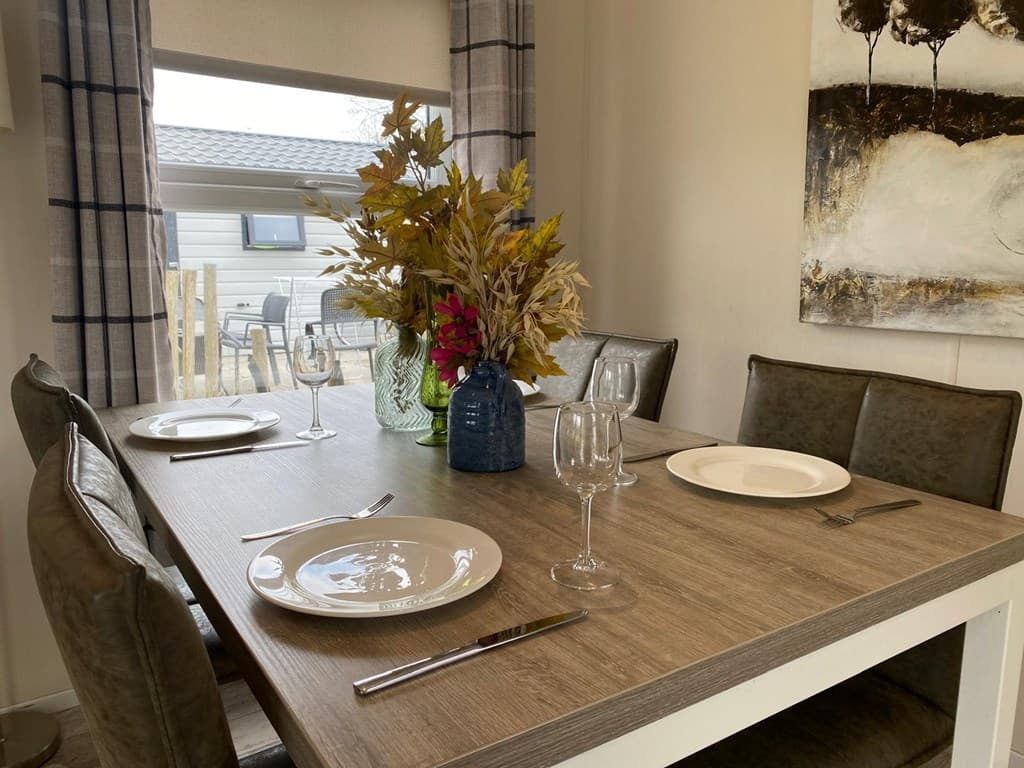 Eettafel met vier borden, glazen en een bloemenvaas in een lichte eetkamer met zicht op buiten.
