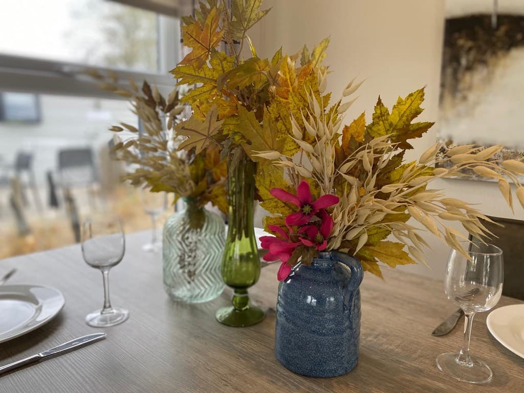 Tafeldecoratie met glazen vazen gevuld met takken en bloemen op een houten tafel met servies in een lichte ruimte