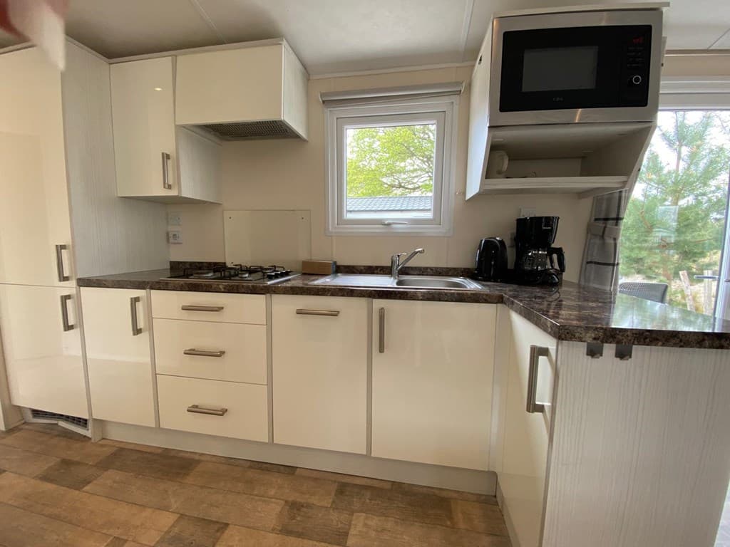 Moderne keuken met lichte kasten, een kookplaat, spoelbak en magnetron tegen een raam voor natuurlijk licht