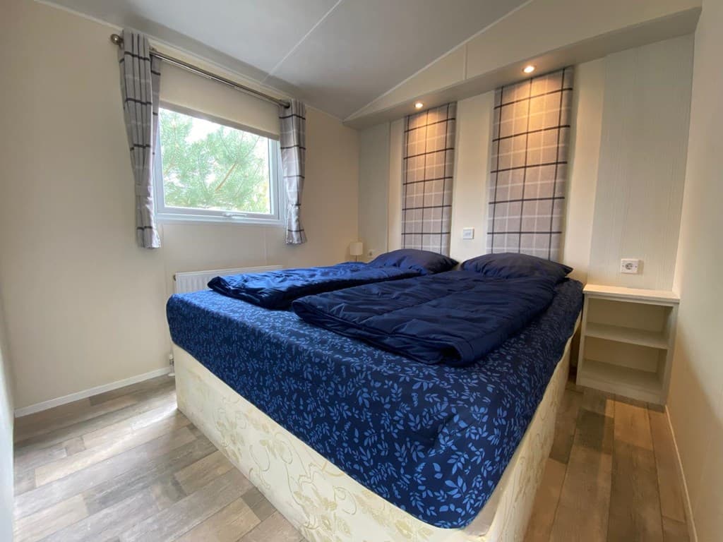 Slaapkamer met twee eenpersoonsbedden, raam met gordijnen en wandlampen, houten vloeren en een nachtkastje