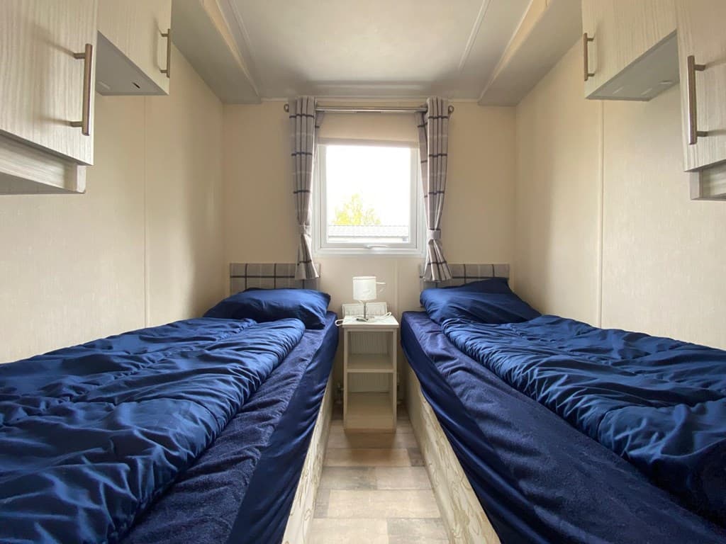 Slaapkamer met twee eenpersoonsbedden en een raam met gordijnen, tussen de bedden staat een nachtkastje.