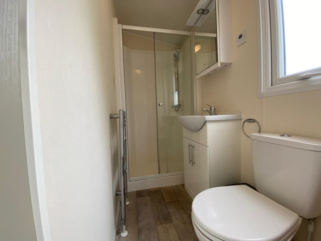 Badkamer met douchecabine, wastafel, toilet en een houten vloer in EuroParcs Zuiderzee.