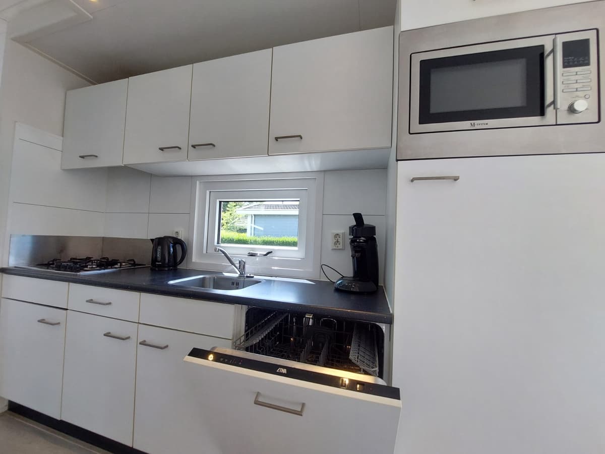 Moderne keuken met ingebouwde apparatuur, waaronder een vaatwasser, magnetron en kookplaat, met uitzicht op de buitenruimte.