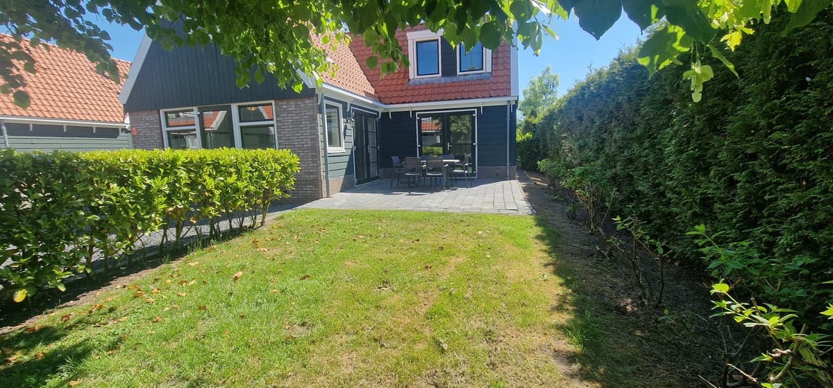 Buitenaanzicht van een woning met een betegeld terras en een groene tuin omgeven door hagen en struiken.