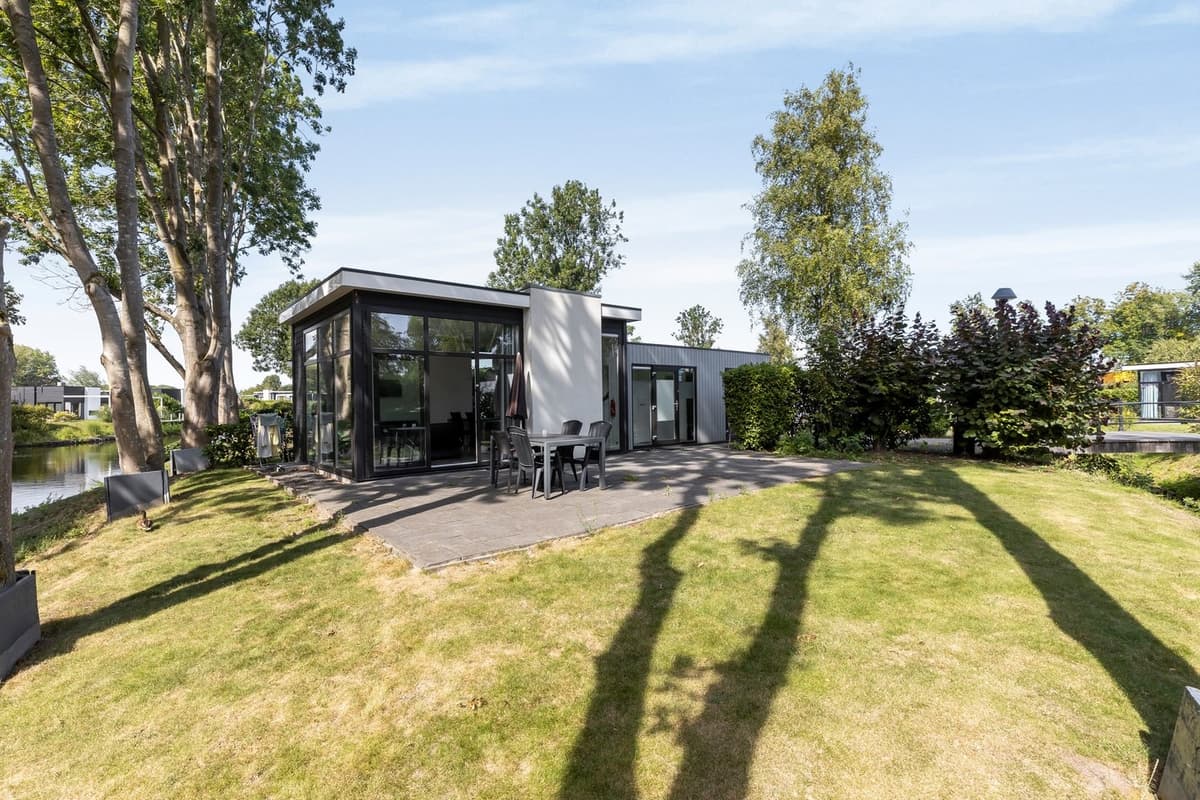 Moderne vakantiewoning met grote ramen, omringd door groen en een bestrate buitenruimte aan het water