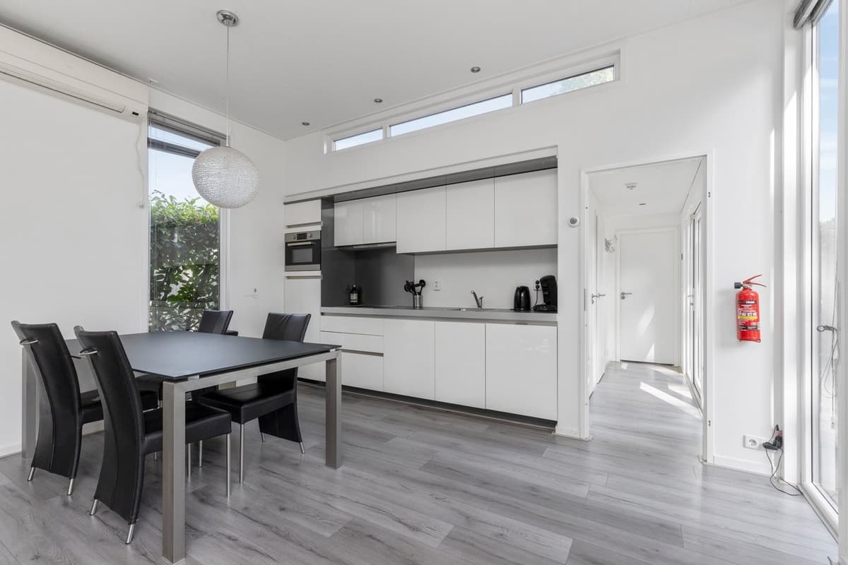 Moderne open keuken met eettafel en zwarte stoelen, veel lichte ruimte door grote ramen.