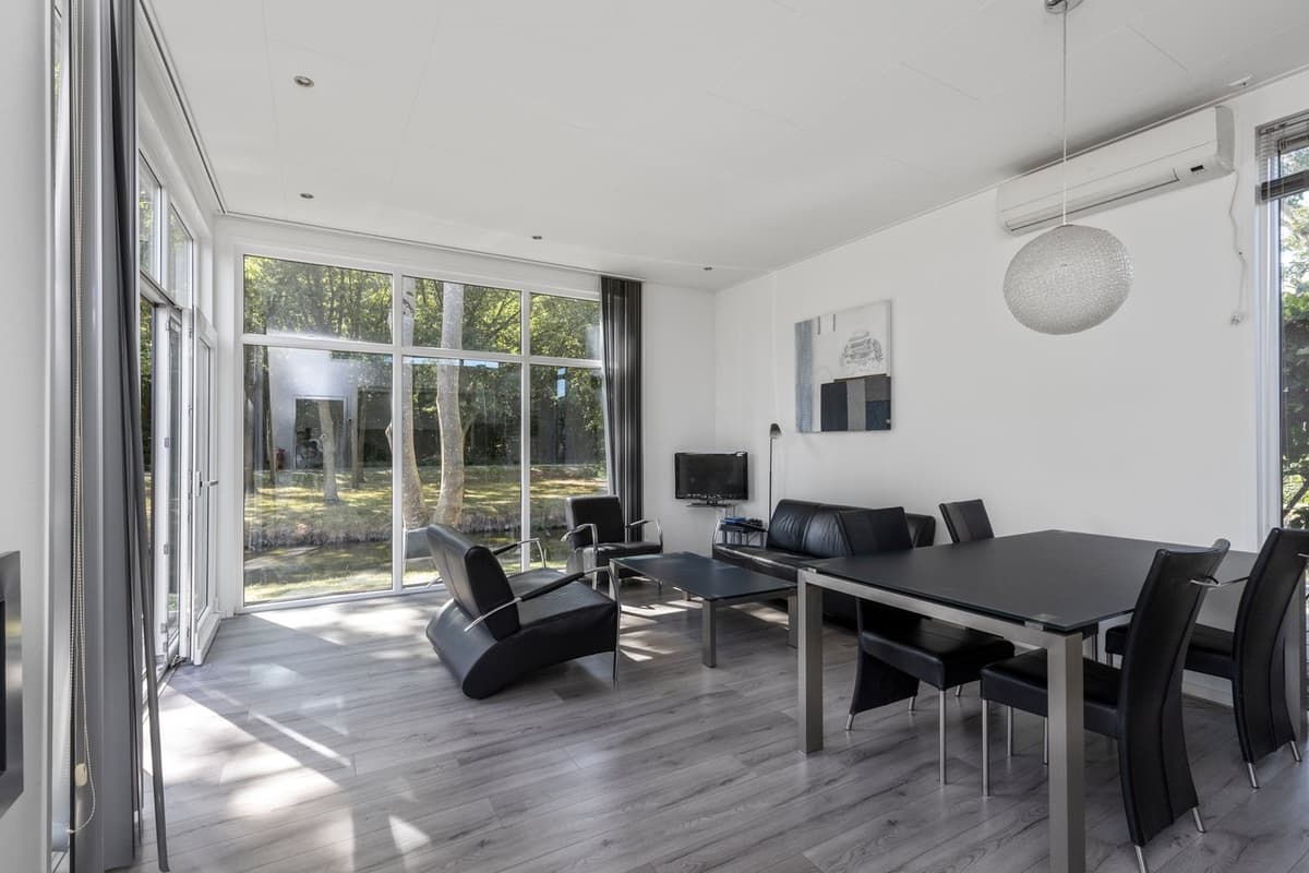 Moderne woonkamer met grote ramen, zwart leren meubilair en uitzicht op een groene tuin.