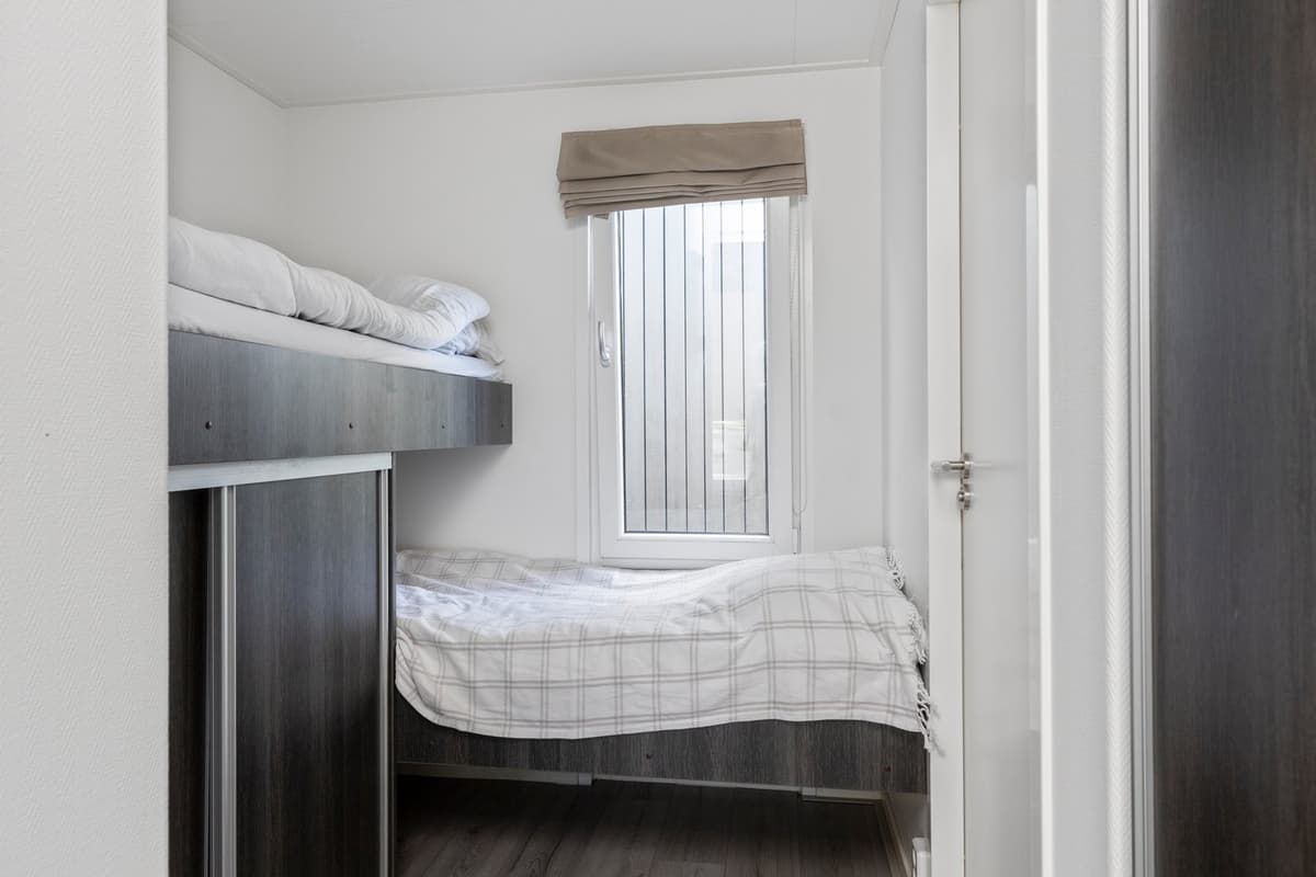 Slaapkamer met stapelbed en raam met jaloezieën, eenvoudige inrichting en lichte muren.
