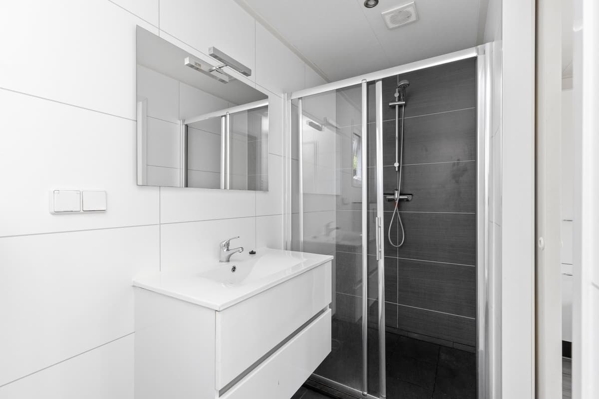 Moderne badkamer met inloopdouche, wastafel met spiegel en lichte wand- en vloerafwerking.