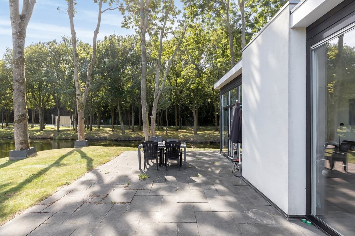 Terras met een eettafel en stoelen, omringd door bomen en uitzicht op een waterpartij