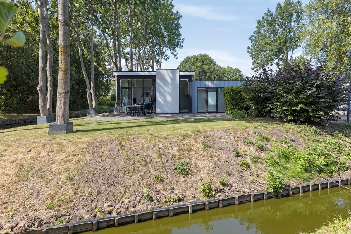 Moderne woning met grote ramen, omringd door bomen en een grasveld, gelegen aan een waterpartij in EuroParcs Spaarnwoude.