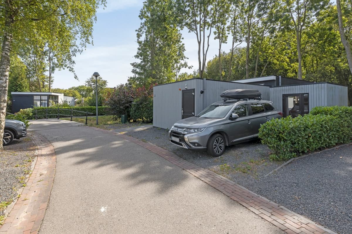 Moderne vakantiewoning met grijs exterieur, gelegen aan een asfaltpad omringd door groen en bomen.