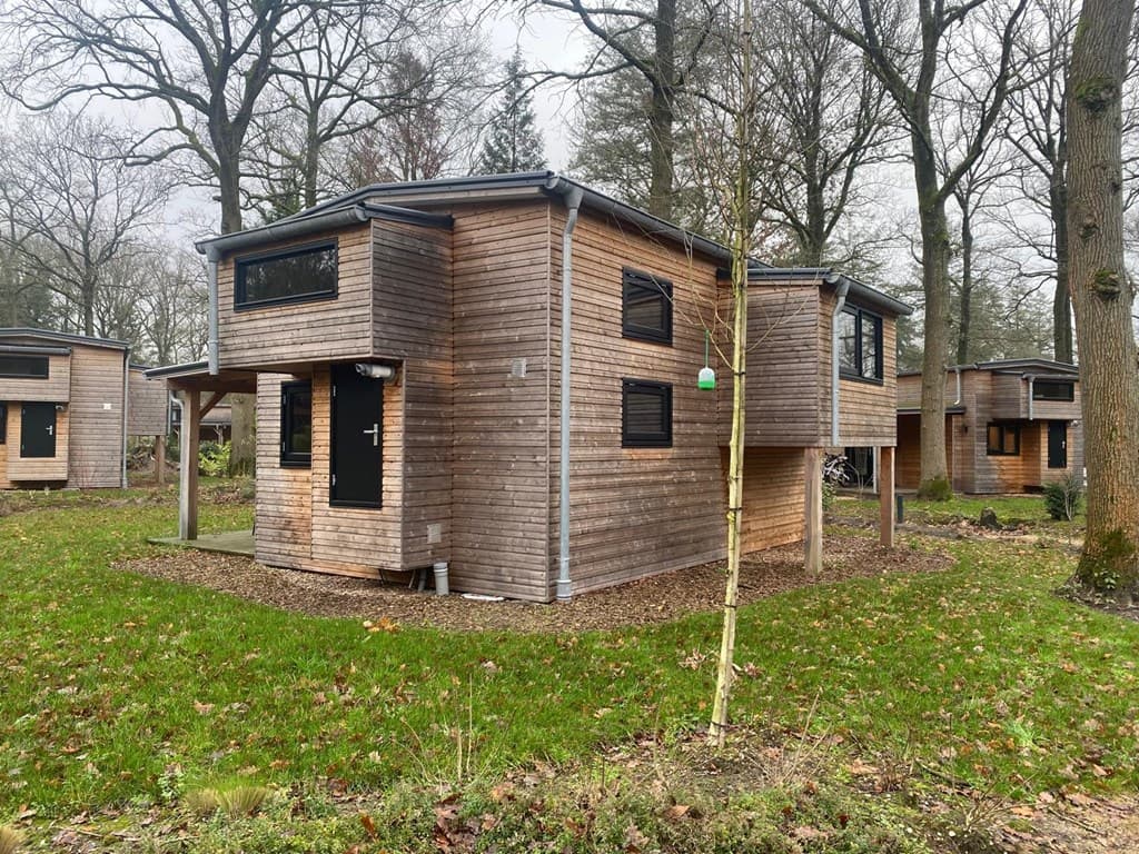 Houten vakantiewoning omringd door bomen en gras op EuroParcs Resort De Utrechtse Heuvelrug in Maarn