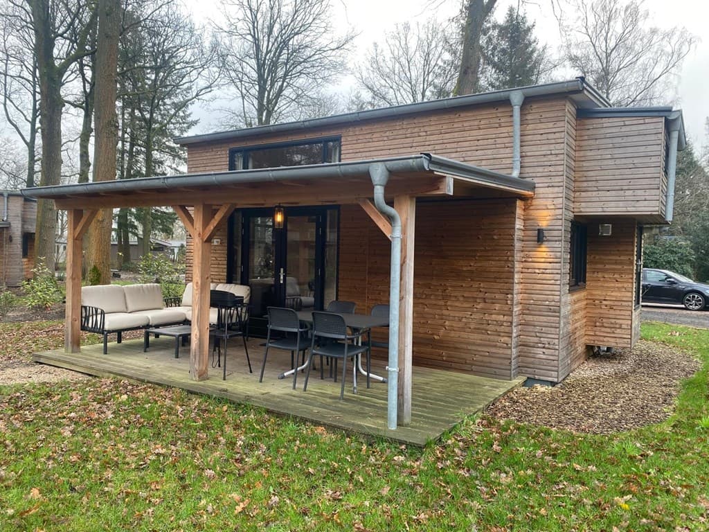 Houten woning met overdekt terras, tuinmeubelen en omgeving met bomen op EuroParcs Resort De Utrechtse Heuvelrug