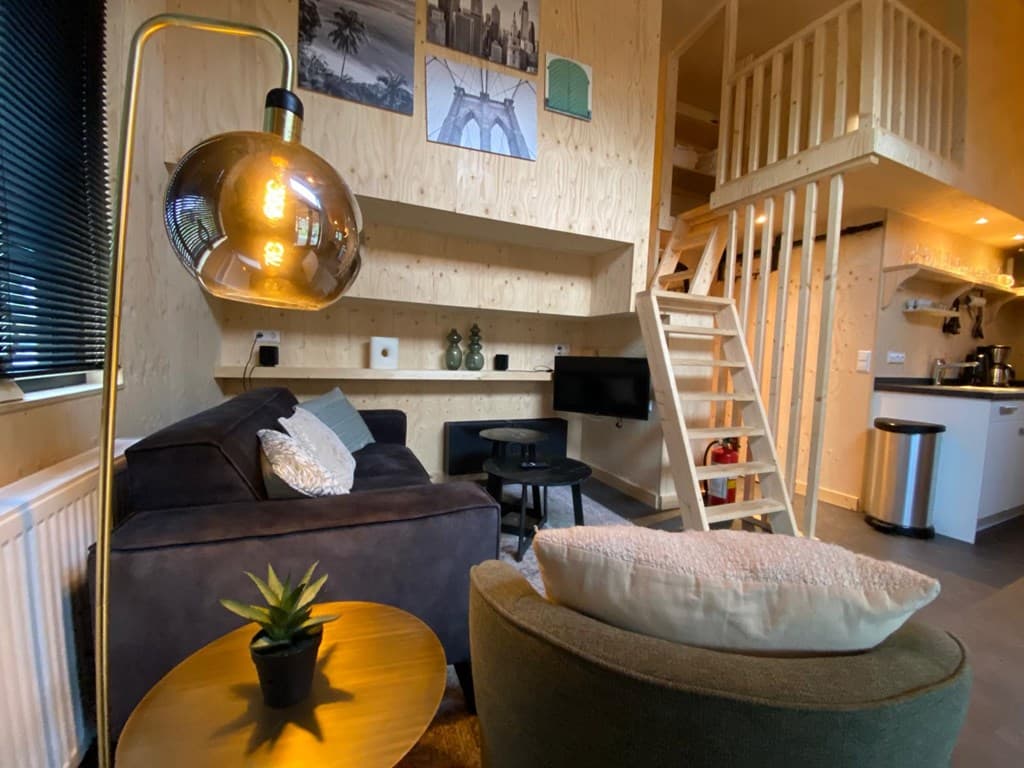 Gezellige woonkamer met houten wand, trap naar boven, zithoek en open keuken met moderne inrichting